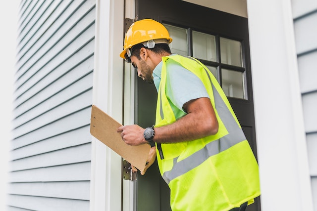 Inspector checking door with clipboard and hard hat.